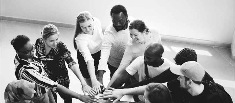 Mixed race group putting their hands together in the center of a circle