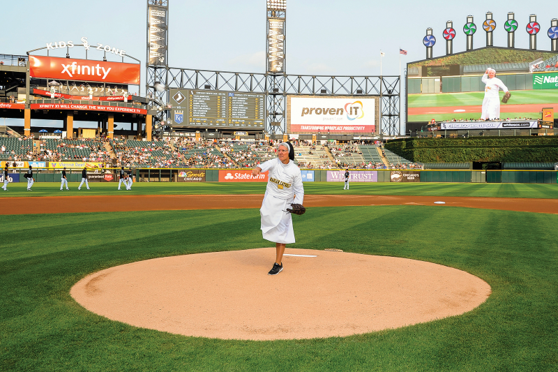 Nun in habit, with school t-shirt over it, and mitt throws from the mound