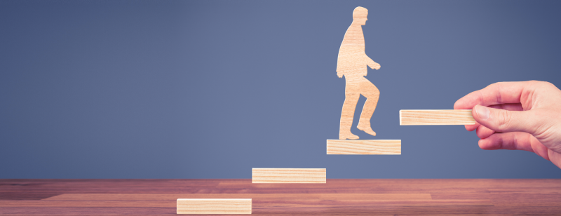 wooden cut-outs of man and stair with last step held by human hand