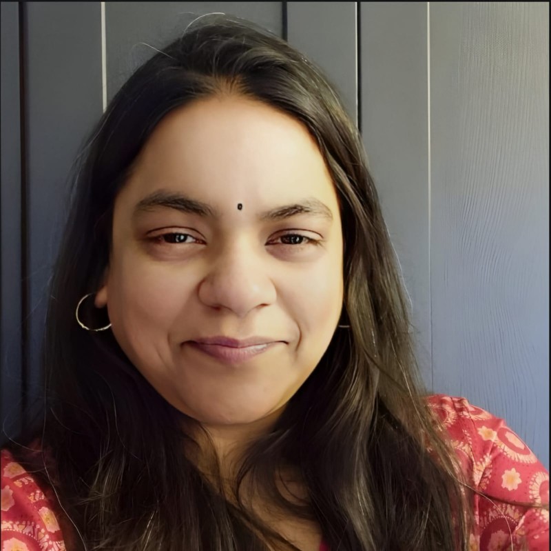 Headshot of Divya Krishnaswamy, a dark-haired Indian woman wearing a red patterned shirt.