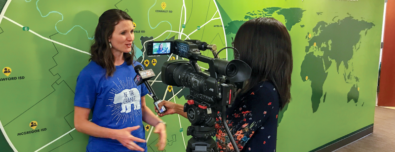 woman in front of map talking to a reporter with a camera and mic
