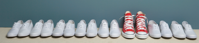 Row of white tennis shoes with one red pair of Chuck's
