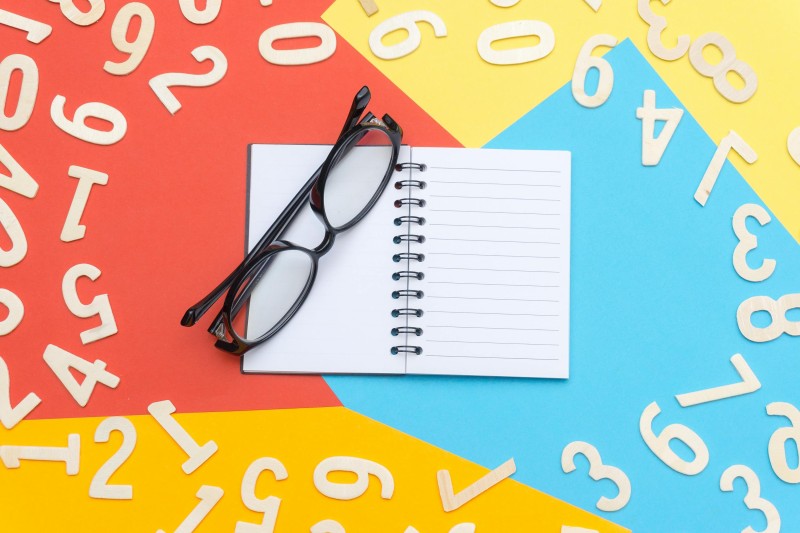 An open notebook and a pair of glasses, with numbers surrounding them.