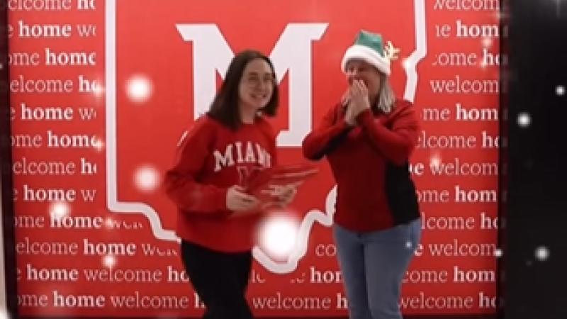 At Miami University, as admissions staff person dressed as an elf hands admissions envelopes to a student wearing a red Miami sweatshirt.
