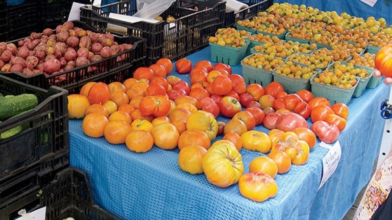 Heirloom tomatoes, cherry tomatoes, and potatoes displayed on tables and in crates at a market.