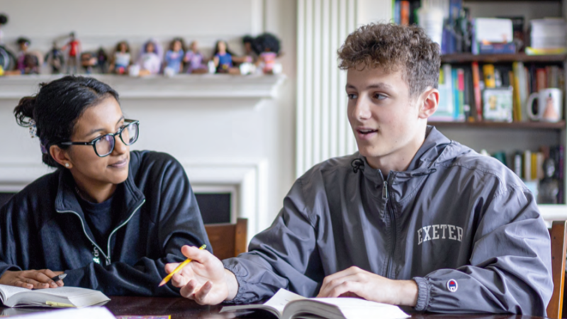 Two Exeter students sit at a table, books open in front of them in discussion.