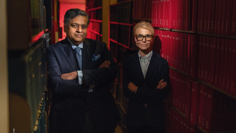 Dr. Kalyanam Shivkumar (left) and Dr. Barbara Natterson-Horowitz (right) each with their arms crossed pose of camera between two rows of bookselves.