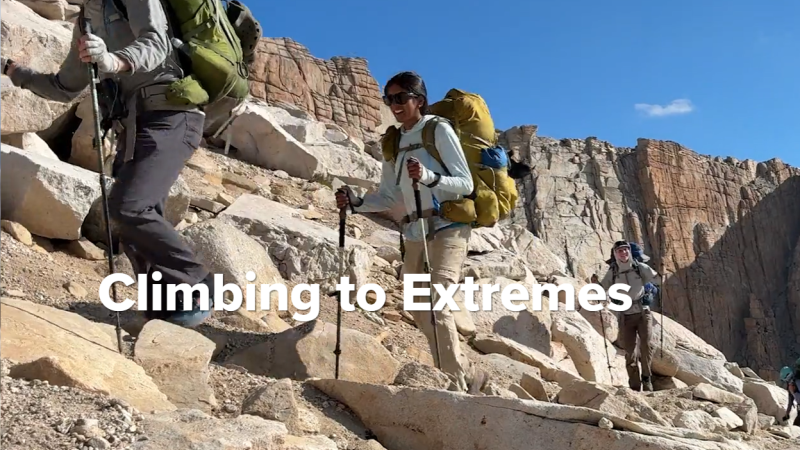 Four hikers climb across a rock formation behind the headline "Climbing to Extremes."