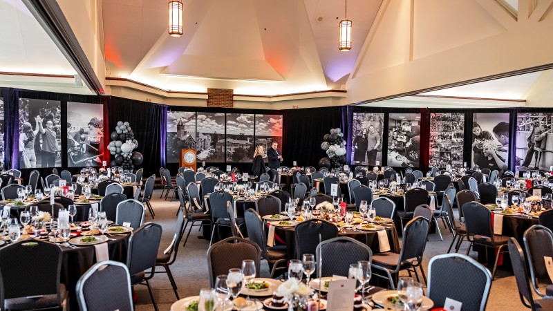 A ballroom is set up for a dinner event. Along the back wall, horizontal black and white photos hang and on the tables salad is served.