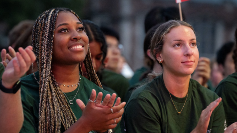 Two Washington University in St. Louis students wearing matching green T-shirts clap at an event.