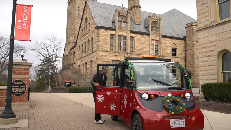 On the Ohio Wesleyan University campus, a red campus cab car, decorated for the holidays with tinsel, lights, and a wreath, picks up a student.