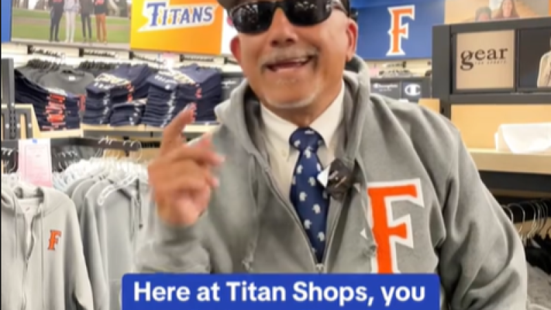 Fullerton's president stands in the university's gift shop wearing university merch. The caption reads, "Here at Titan Shops, you can find your Titan Drip."