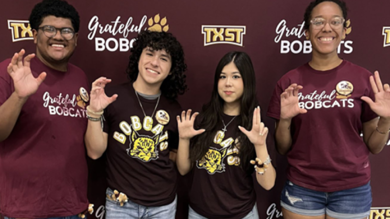 Four TXST students pose for a photo, holding their hands up in claw-like pose.