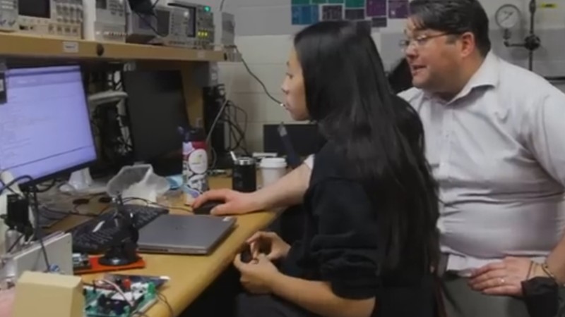 A student and instructor sit at a computer in a mechanical engineering lab.
