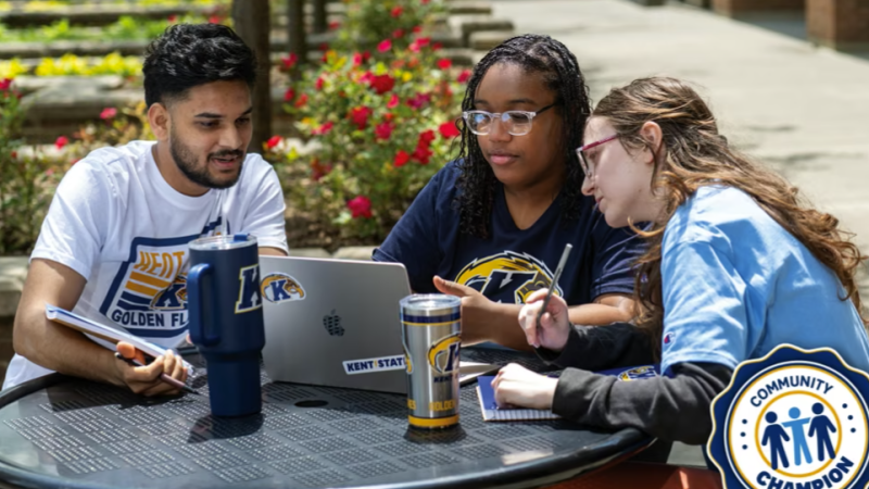 A photo of three Kent State students sitting around a table outside on campus doing homework.