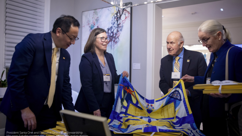 Two U-M advancement staff present the Catalyst scarf to two donors.