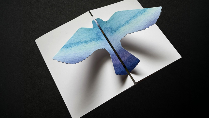 A white invitation with a blue-ombre-colored bird pop-out.