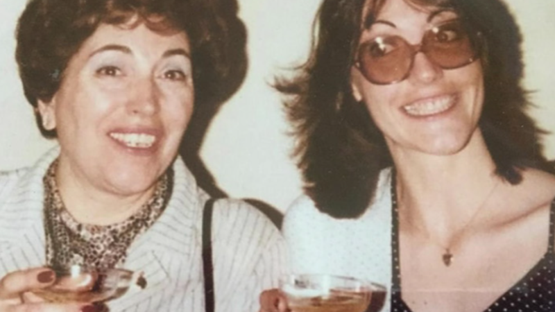 A mother and daughter smile for the camera. Each holds a coupe glass filled with a pink colored drink.