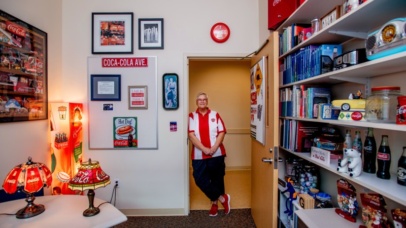 A person standing in the doorway of their office filled with Coca-Cola memorabilia.