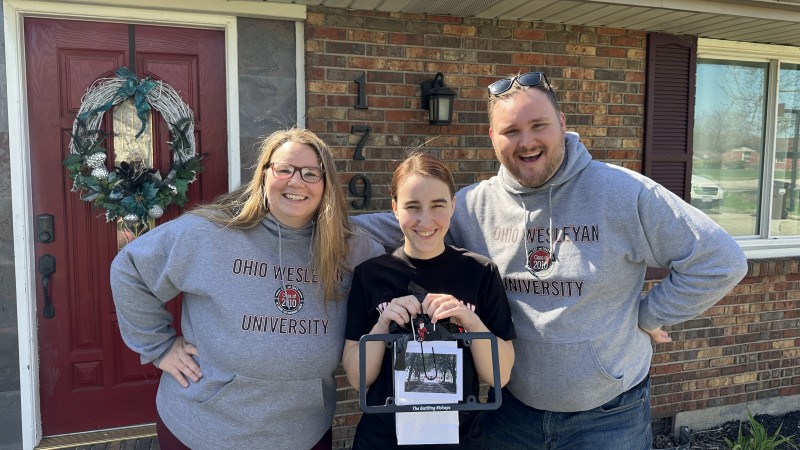 Two people wearing matching gray Ohio Wesleyan University Class of 2010 sweatshirts pose with a prospective student holding a goody bag.
