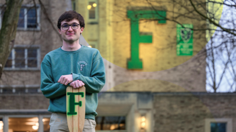 A photo of Ryan Murphy '26 standing in front of Notre Dame's Fisher Hall holding an oar with a green "F" on it.