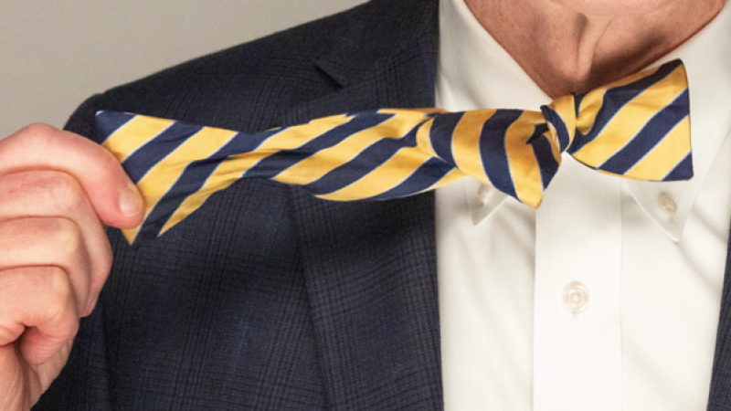 The cover of the Spring/Summer 2025 issue of the Peddie Chronicle features a close-up of Peter Quinn removing the blue and yellow striped bow tie at his collar with his right hand.