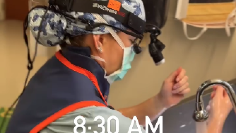 A medical resident scrubs in for surgery. She wears a light blue scrub cap with turtles on it.