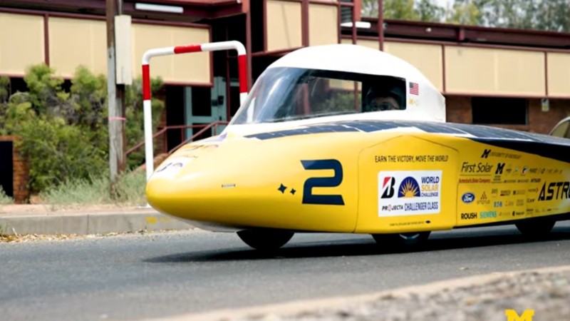 University of Michigan's yellow solar car moves down an urban street.