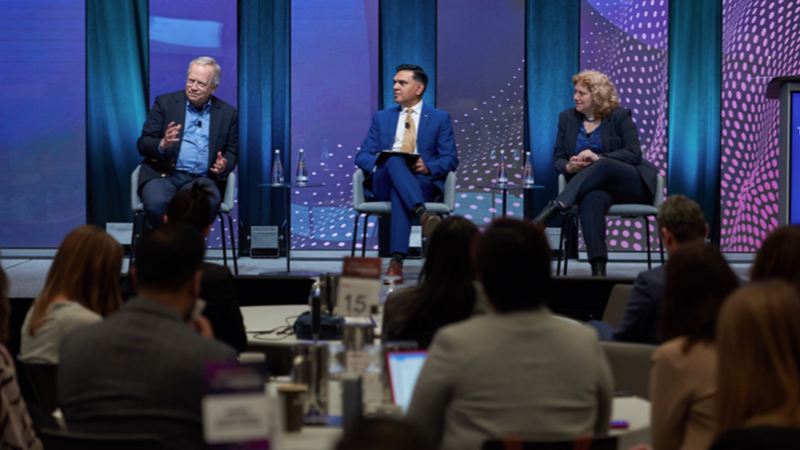 At Tech Horizons, three people sit in chairs on stage in front of a crowd seated at circular tables.
