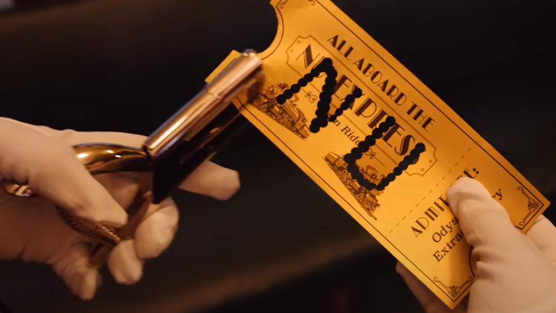 A close-up of two white gloved hands. One holds a hole punch. The other holds a gold ticket for the NU Express with the letters "N" and "U" hole-punched in its center.