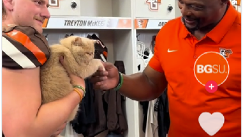 A screenshot from a BGSU TikTok shows a football coach shaking the paw of a cat being held by a football player.