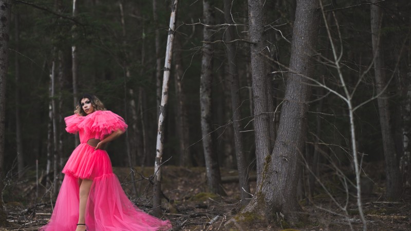 Jaime Aranzabal, dressed in a bright pink dress, stands in the middle of the woods.
