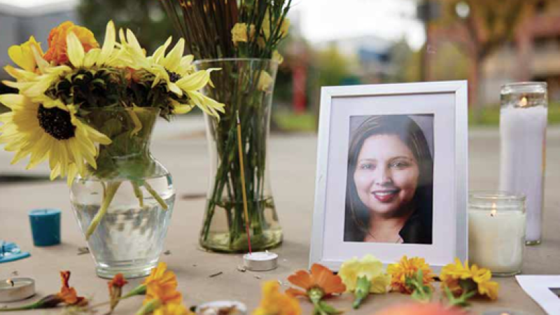 A portrait of Patricia Navarro Velez sits on the ground amongst flowers and candles.