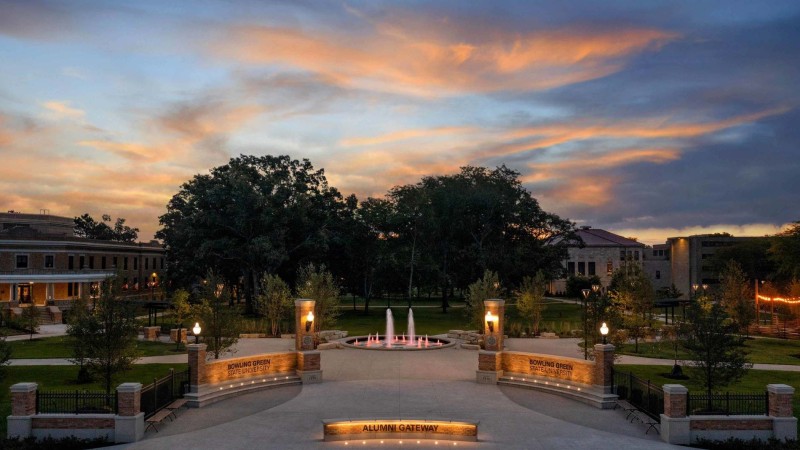 A photo of Bowling Green State University campus at night, an orange and blue sunset in the sky. At center, a fountain surrounded by brick campus buildings.