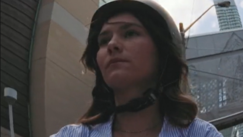 Through a fisheye lens, a close-up of a TMU student riding a bike through Toronto. She wears a black helmet.