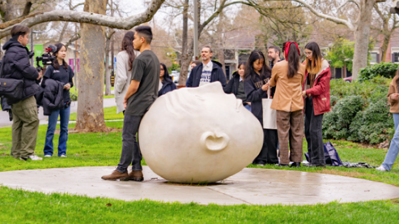 UC Davis students gather around one of the Egghead statues. One student leans against the head to pose for a picture.