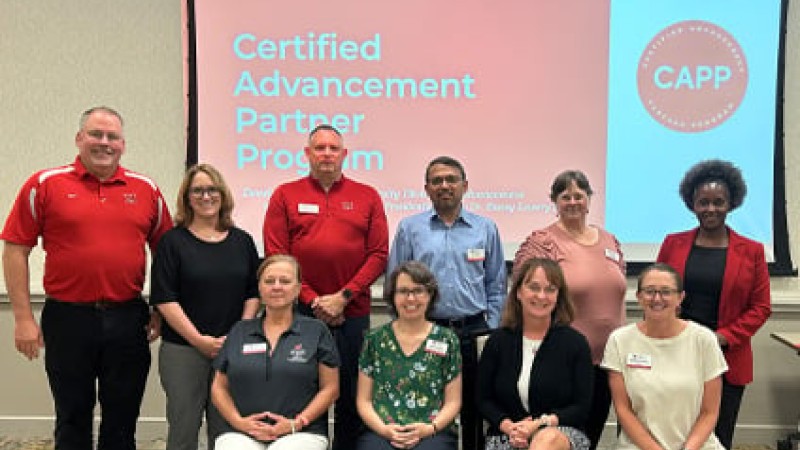 A cohort poses for a photo in two rows in front of a presentation screen that reads "Certified Advancement Partner Program."